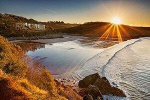 Dan Santillo Glass Placemat - Toughened, Felt-Backed featuring Caswell Bay beach at sunset with golden sunlight reflecting on the water. Durable 22.5x18.5cm placemat with scenic coastal photo and protective felt backing.