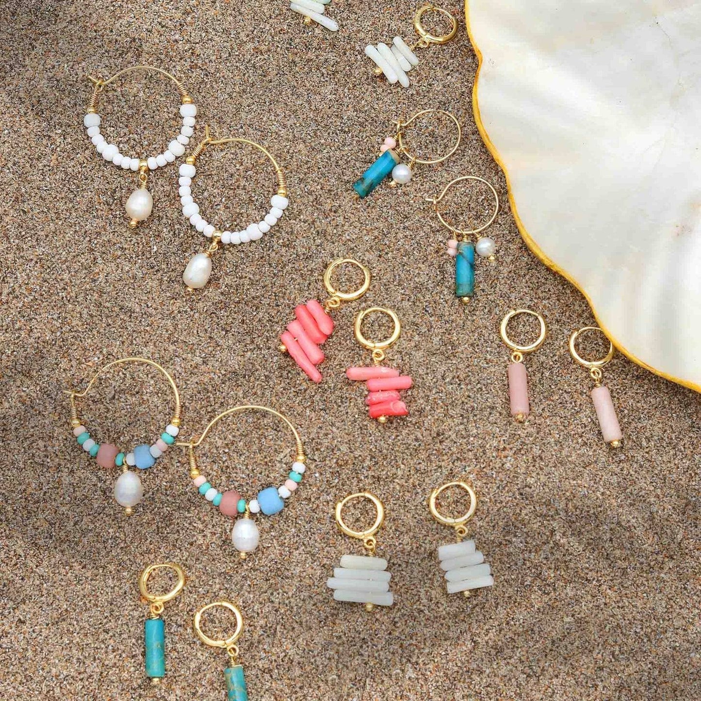 GIADA GEGAMBAR WIRE HOOP EARRINGS displayed on sand with colorful beaded earring collection and shell dish.