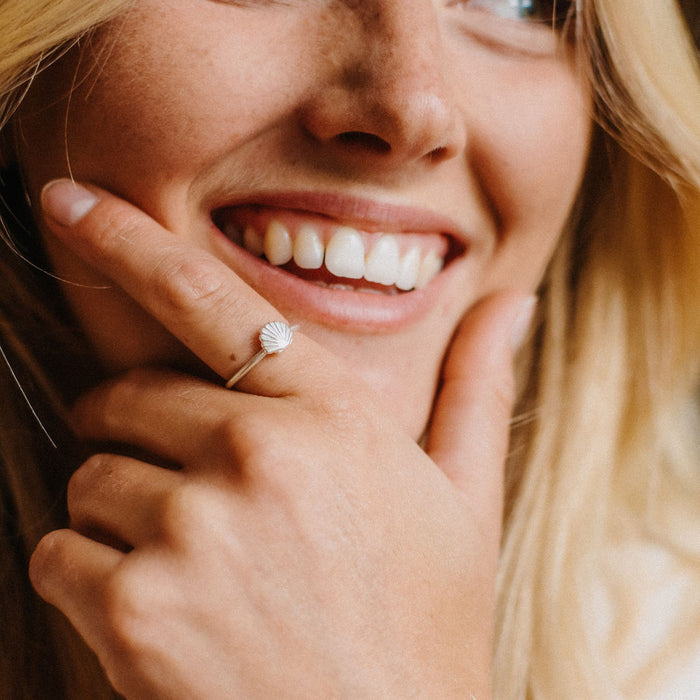 Woman smiling while wearing a silver adjustable shell ring, beach-inspired jewelry.