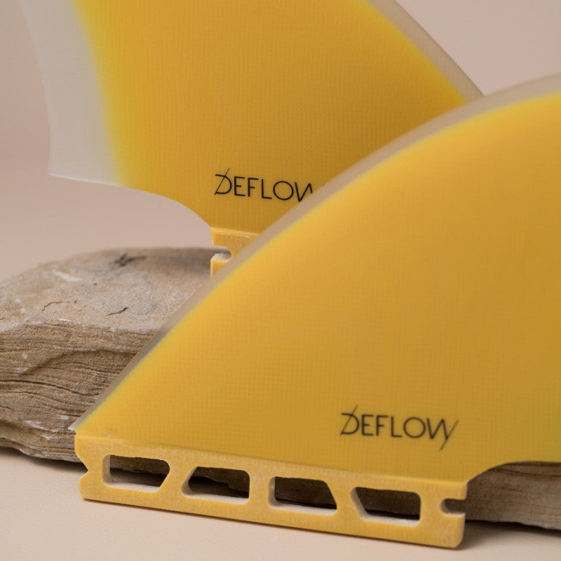 Detailed view of Deflow Palm twin fins in mustard color on a stone base.