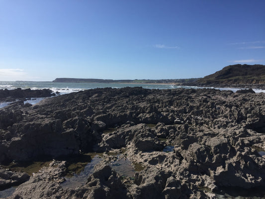 Rocky coastline under a clear blue sky with waves crashing in the distance.
