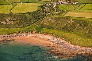 Dan Santillo Glass placemat - Slade features an aerial photo of Slade Bay with sandy beach, rocky shoreline, and lush green fields above the cliffs.