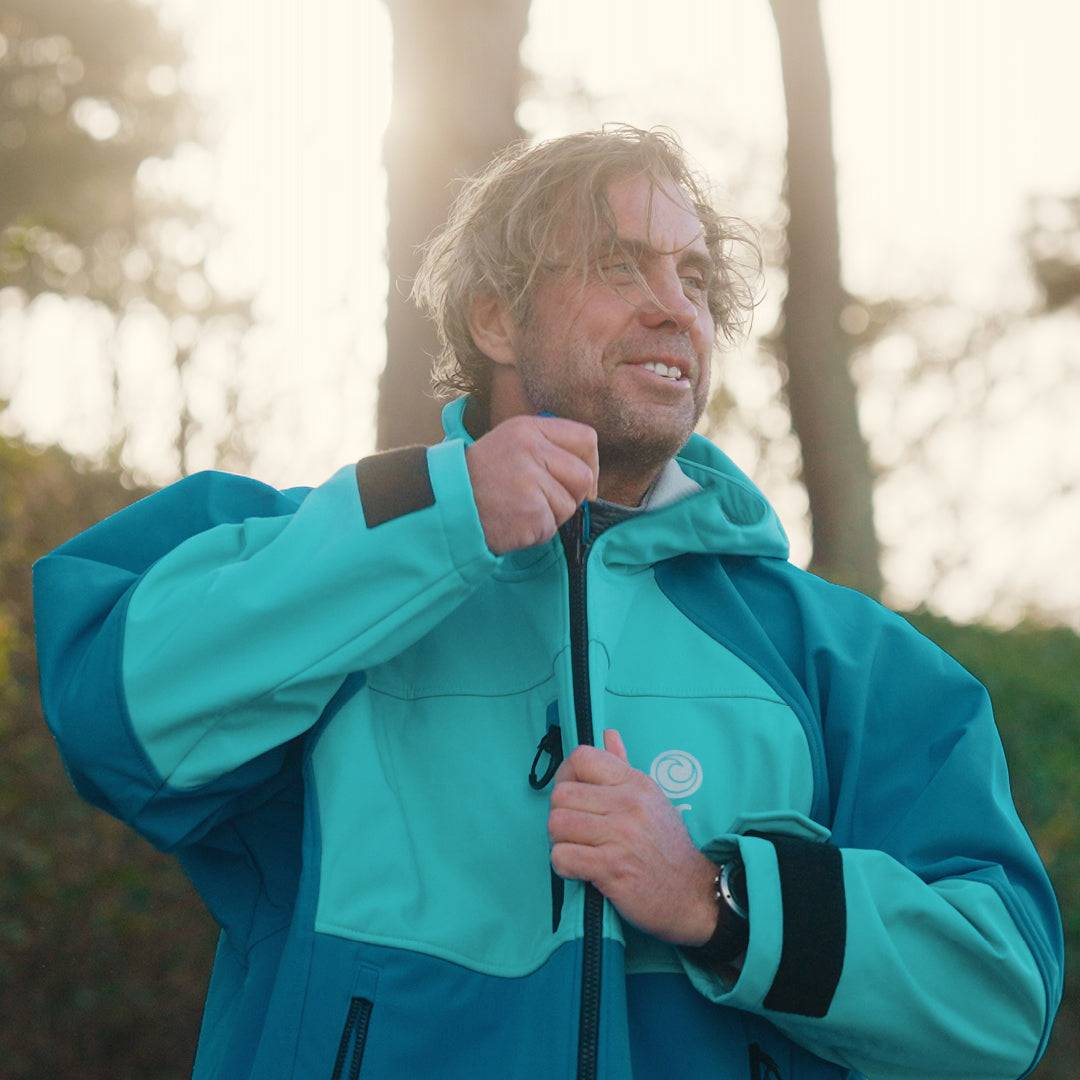 Man zipping up the White Water cobalt blue soft shell robe outdoors, highlighting its durable design.