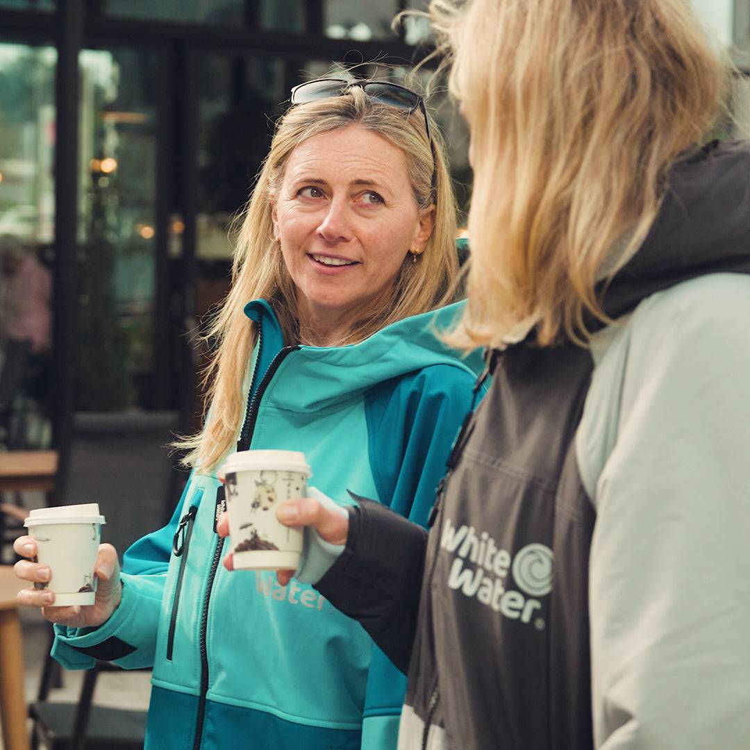 Two women enjoying coffee while wearing White Water soft shell robes, one in cobalt blue and the other in gray.