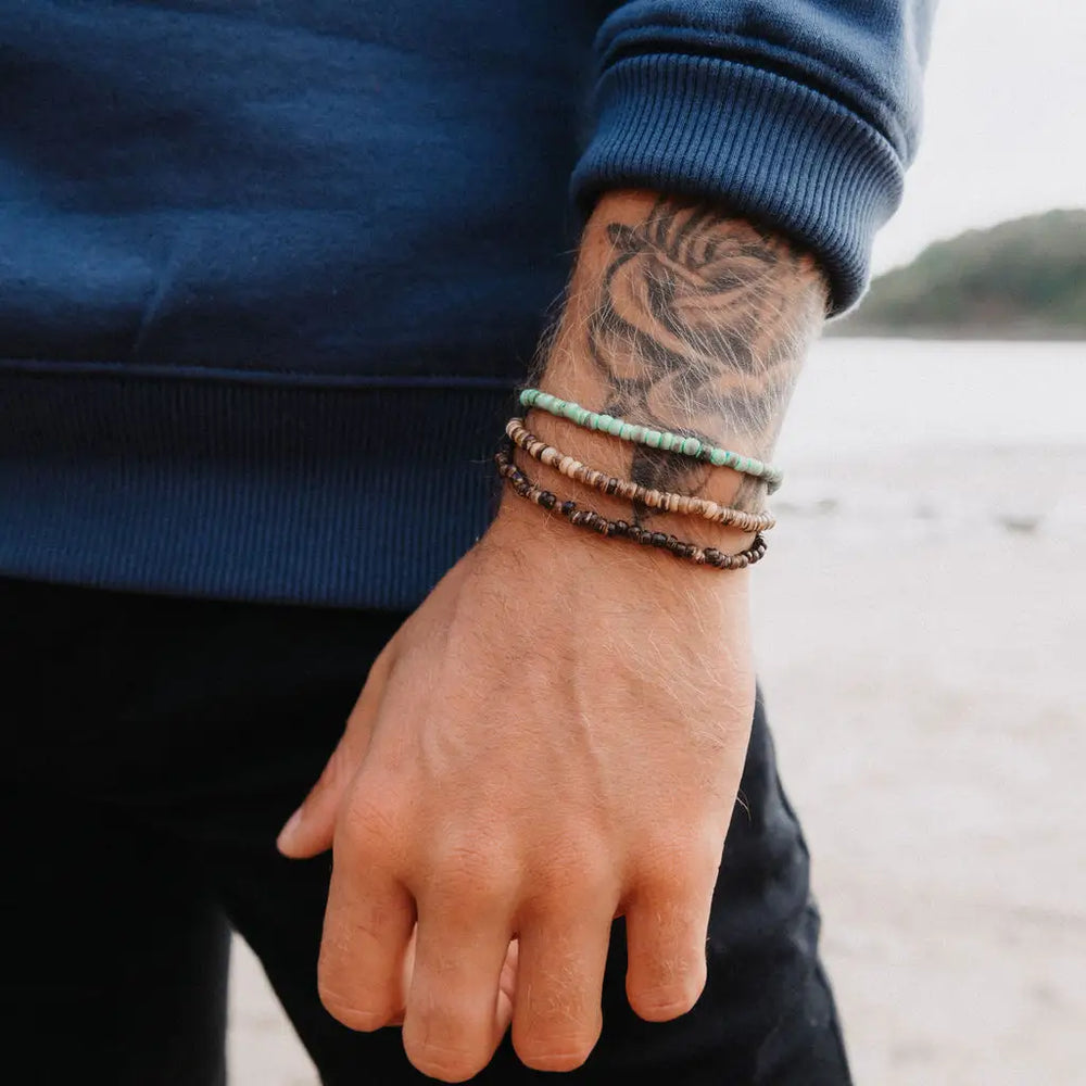 Man wearing layered bracelets, including the green Coconut Beach Bracelet.