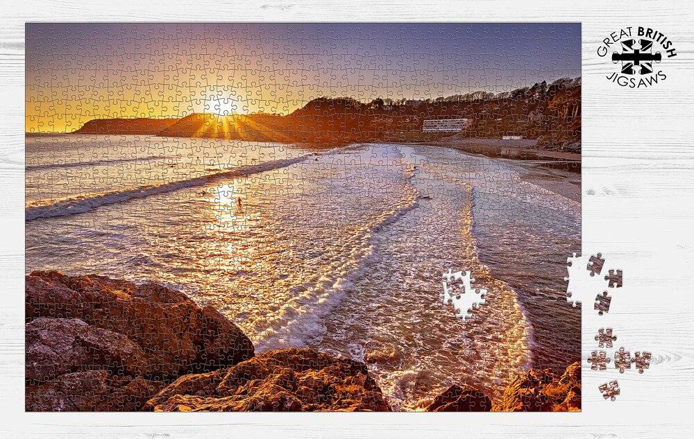 Completed Dan Santillo jigsaw puzzle of Caswell Bay sunset with scattered pieces.