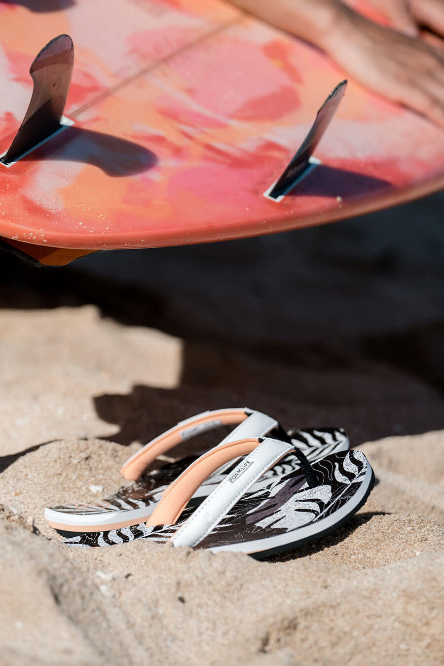 FoamLife Zikat SC flip flops on sandy beach near a surfboard.