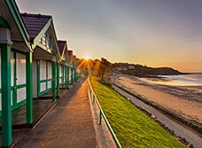 Dan Santillo greeting card featuring Langland beach huts at sunrise.