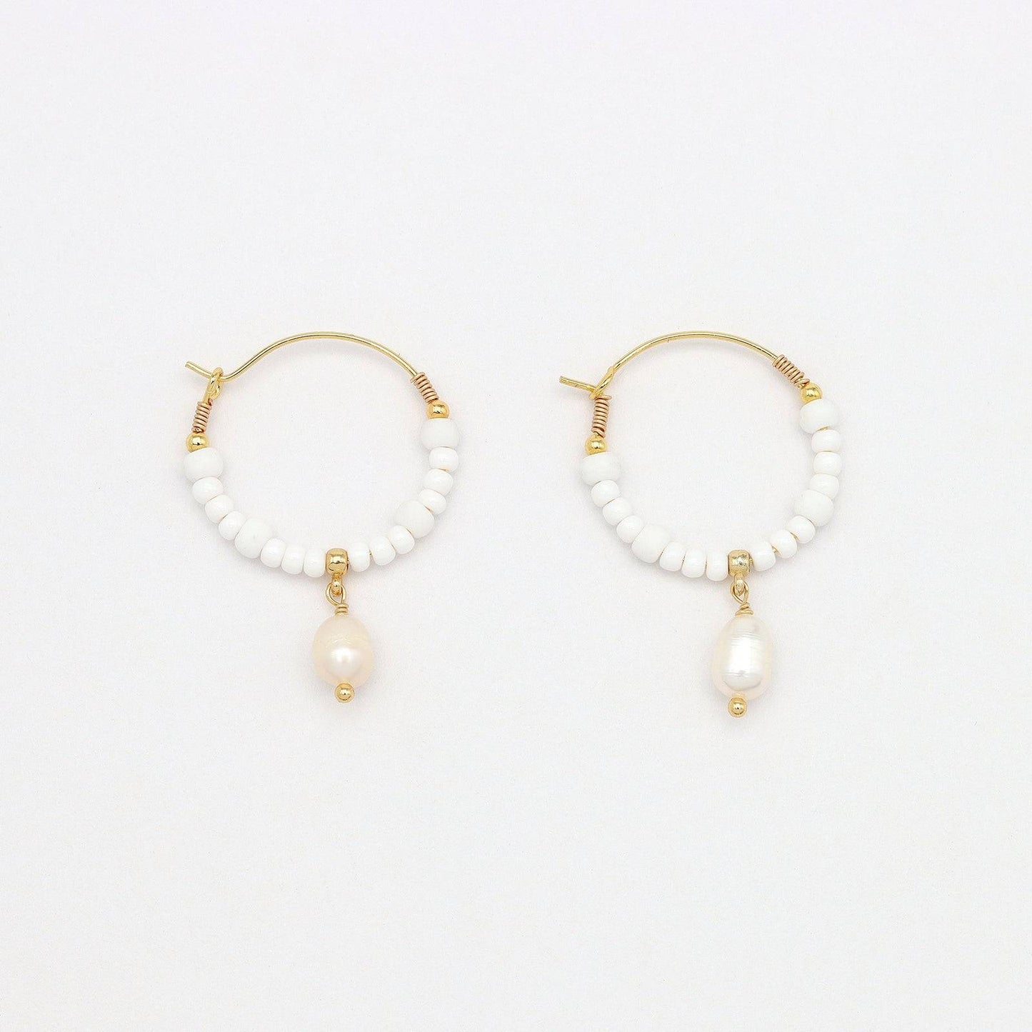 Pair of GIADA GEGAMBAR WIRE HOOP EARRINGS featuring white beading and pearl drop charm laid flat on a white surface.