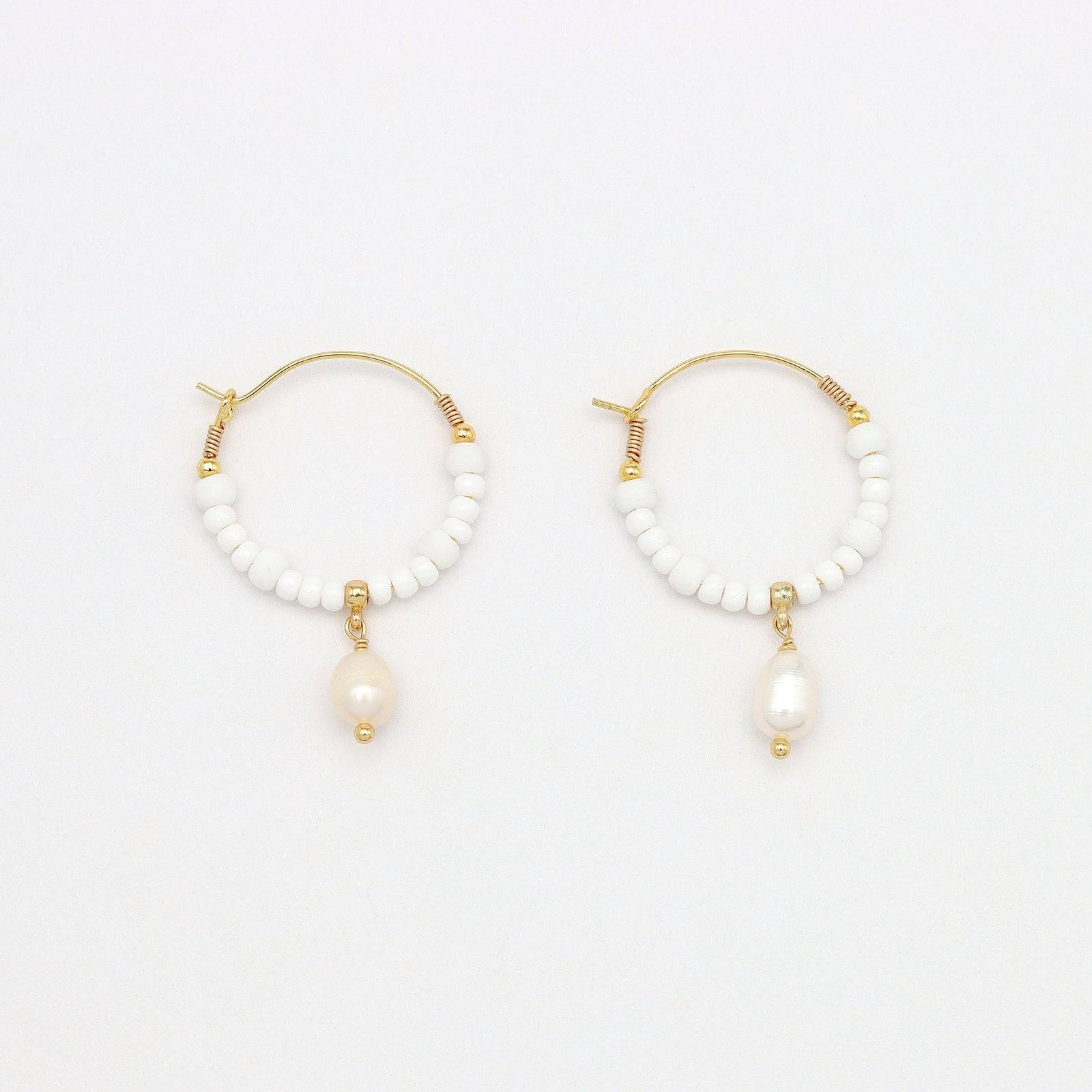 Pair of GIADA GEGAMBAR WIRE HOOP EARRINGS featuring white beading and pearl drop charm laid flat on a white surface.