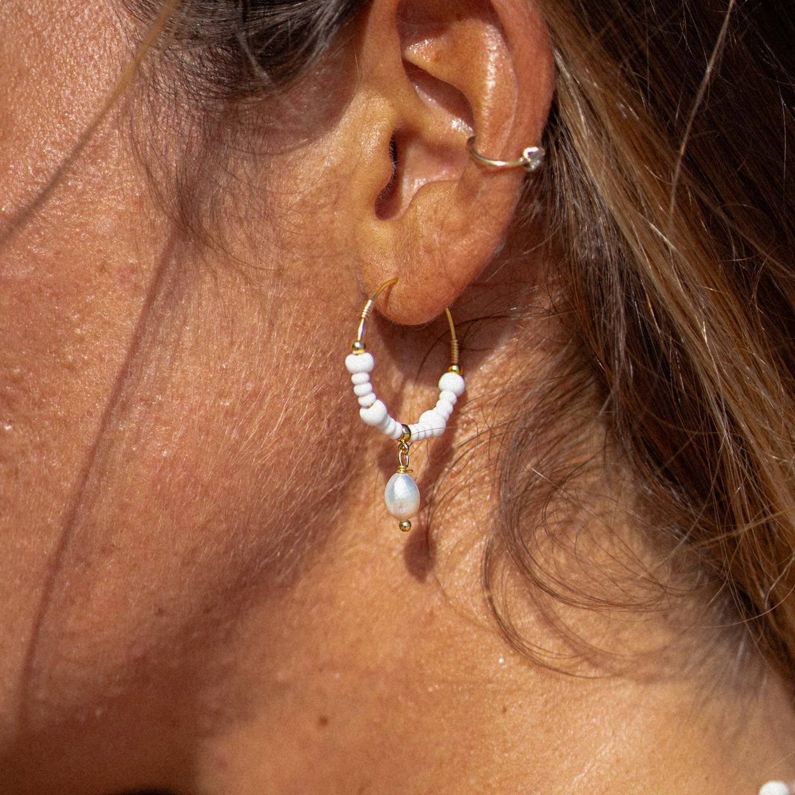 GIADA GEGAMBAR WIRE HOOP EARRINGS worn on ear, showcasing white beaded hoops with central pearl charm in natural sunlight.
