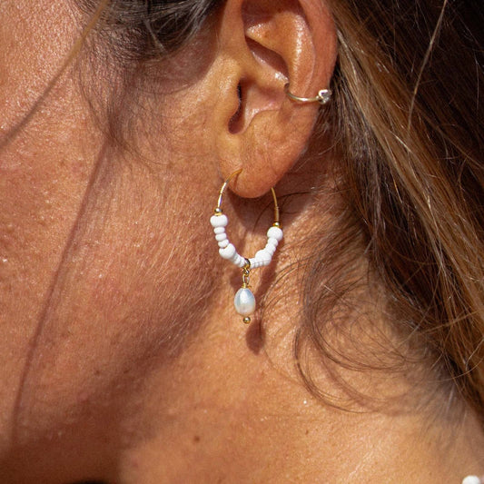 GIADA GEGAMBAR WIRE HOOP EARRINGS worn on ear, showcasing white beaded hoops with central pearl charm in natural sunlight.
