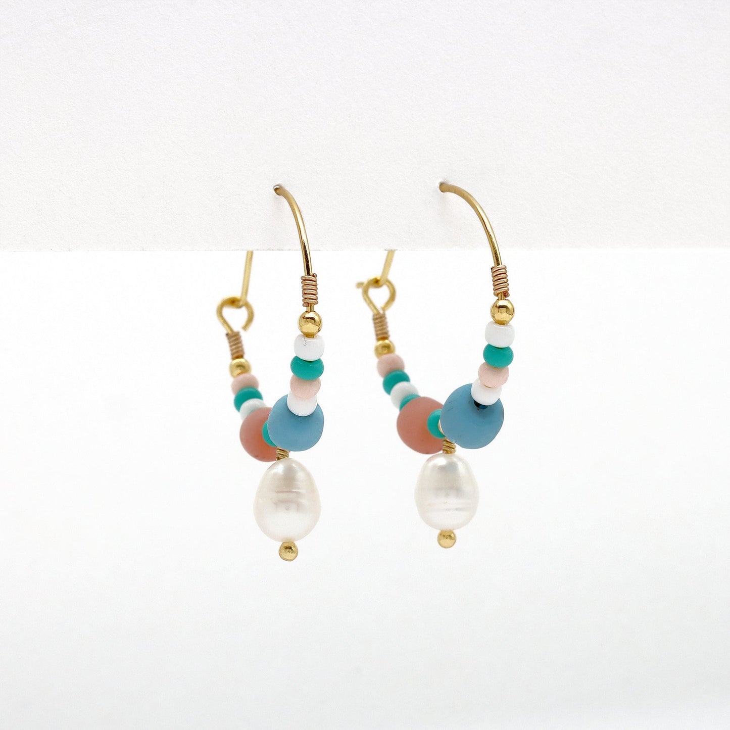 Side view of GIADA PECAHAN WIRE HOOP EARRINGS with colorful beads and pearl charm, suspended from gold hoops for a vibrant finish.