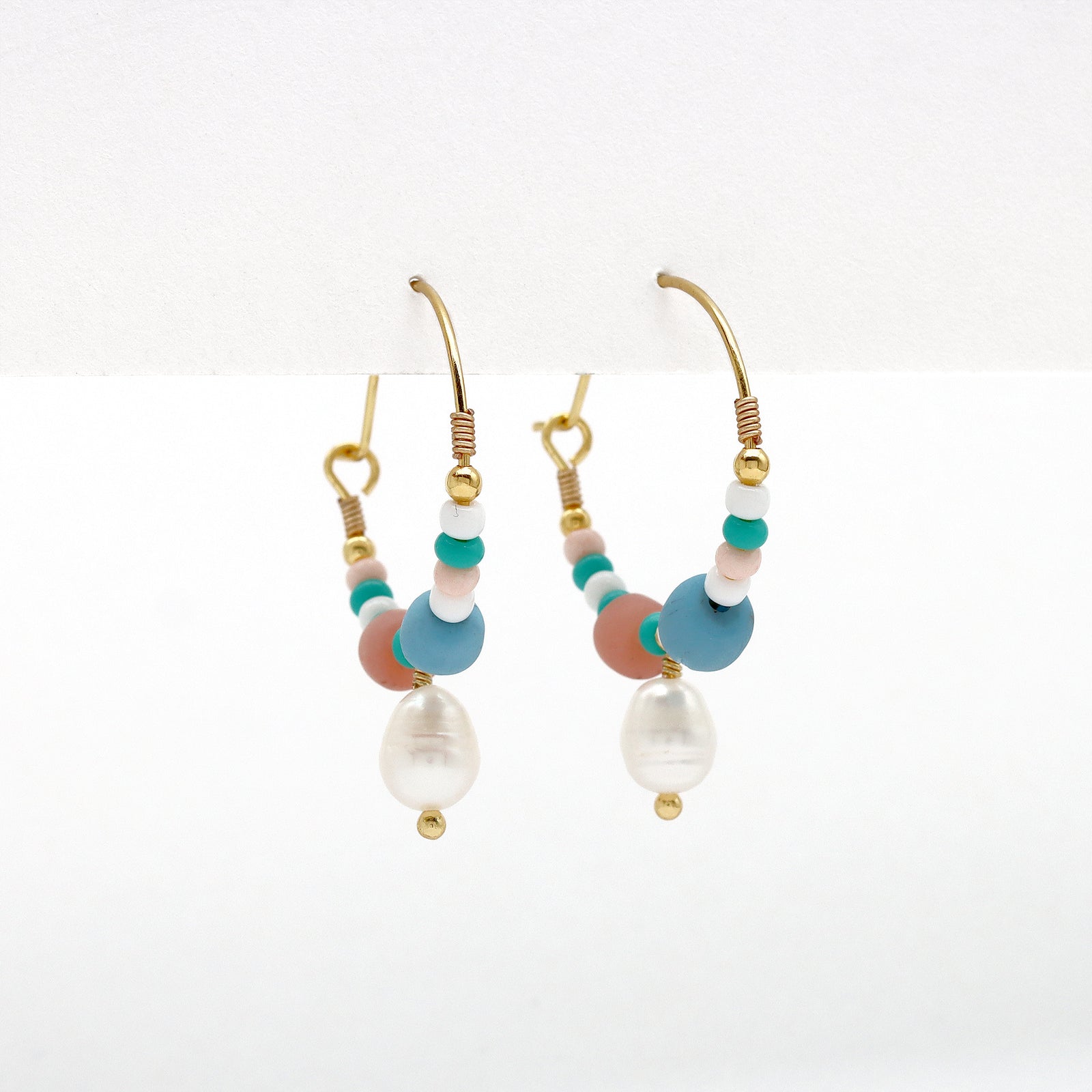Side view of GIADA PECAHAN WIRE HOOP EARRINGS with colorful beads and pearl charm, suspended from gold hoops for a vibrant finish.