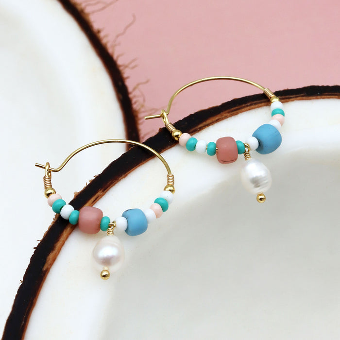 GIADA PECAHAN WIRE HOOP EARRINGS resting on ceramic dish, featuring pastel beads and pearl charm for a delicate, feminine style.