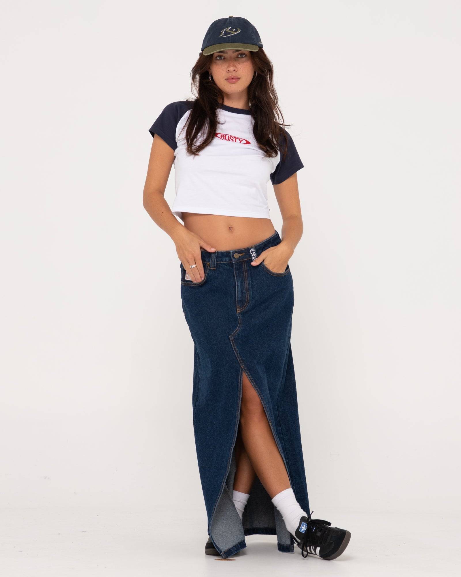 Rusty Celeste low-rise denim maxi skirt styled with a cropped top and cap.