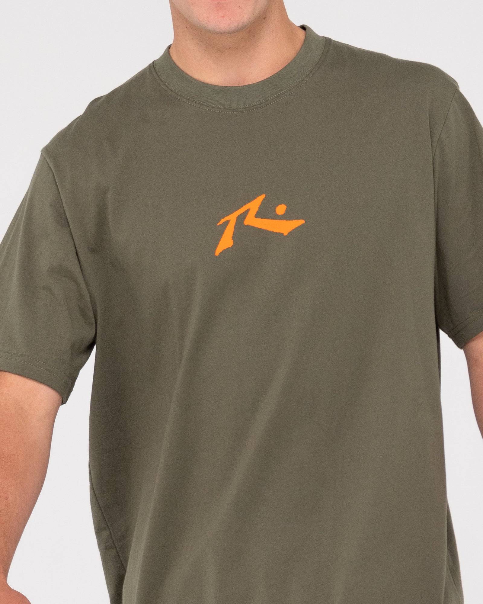 Close-up of Rusty One Hit CF Competition tee with orange logo on olive green fabric.