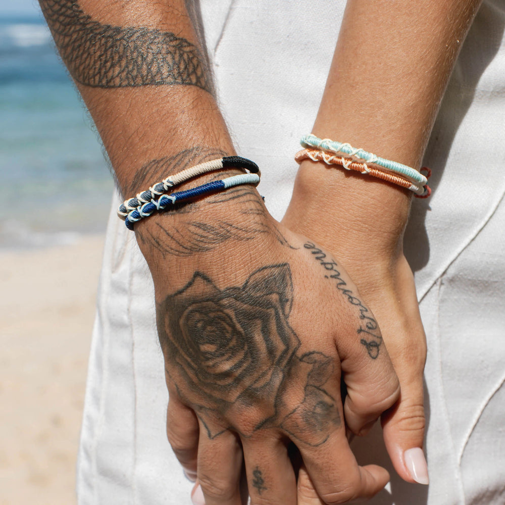 Couple holding hands wearing Pineapple Island Rapture Woven Bracelets on a beach.