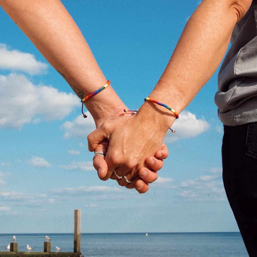 Two people holding hands wearing Pineapple Island woven pride bracelets.