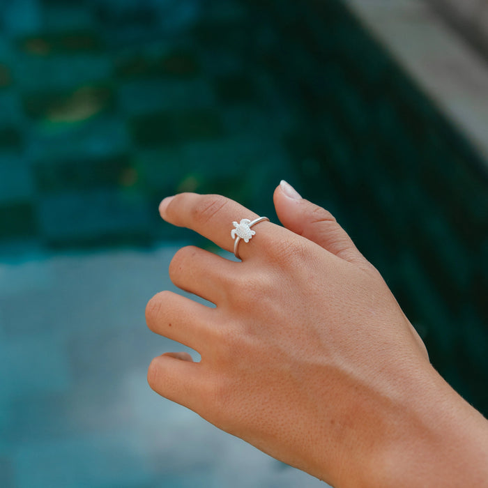 Silver adjustable turtle ring worn on a hand near a pool.