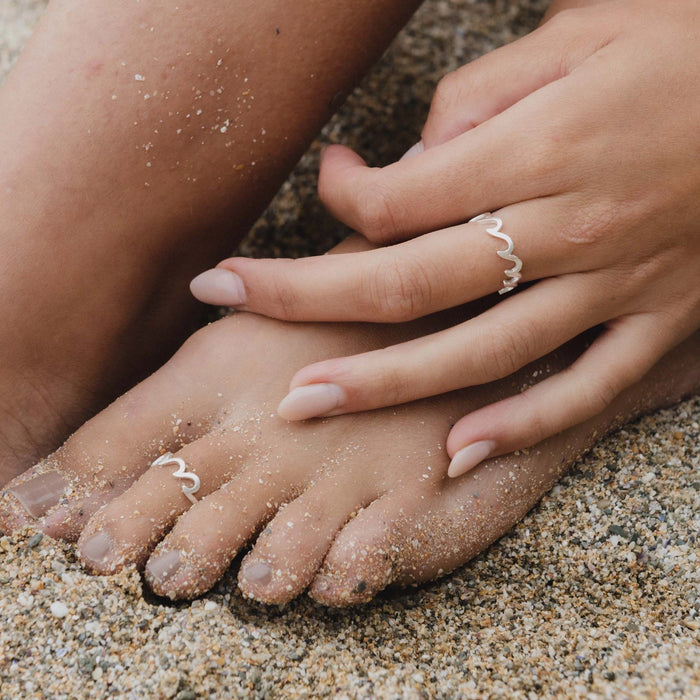 Silver Crashing Wave Ring worn on hand and toe on sandy beach.