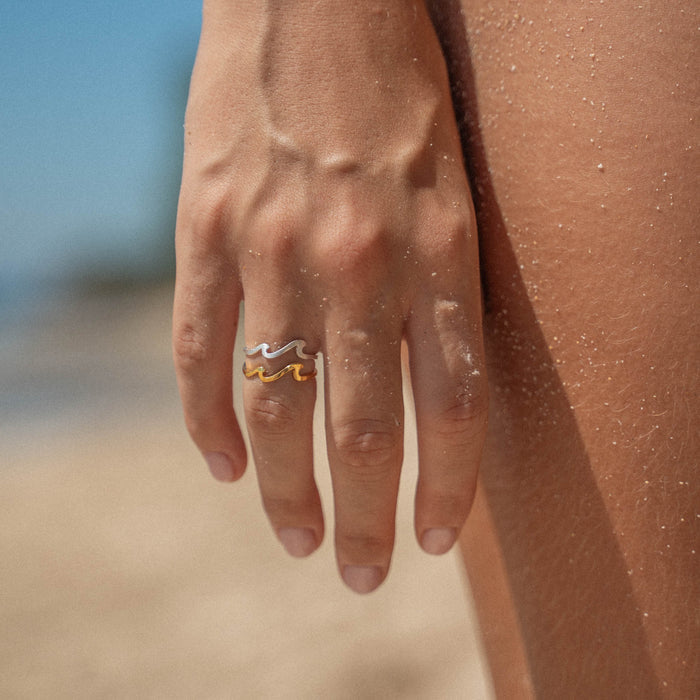 Gold double wave ring worn on a sandy hand at the beach.