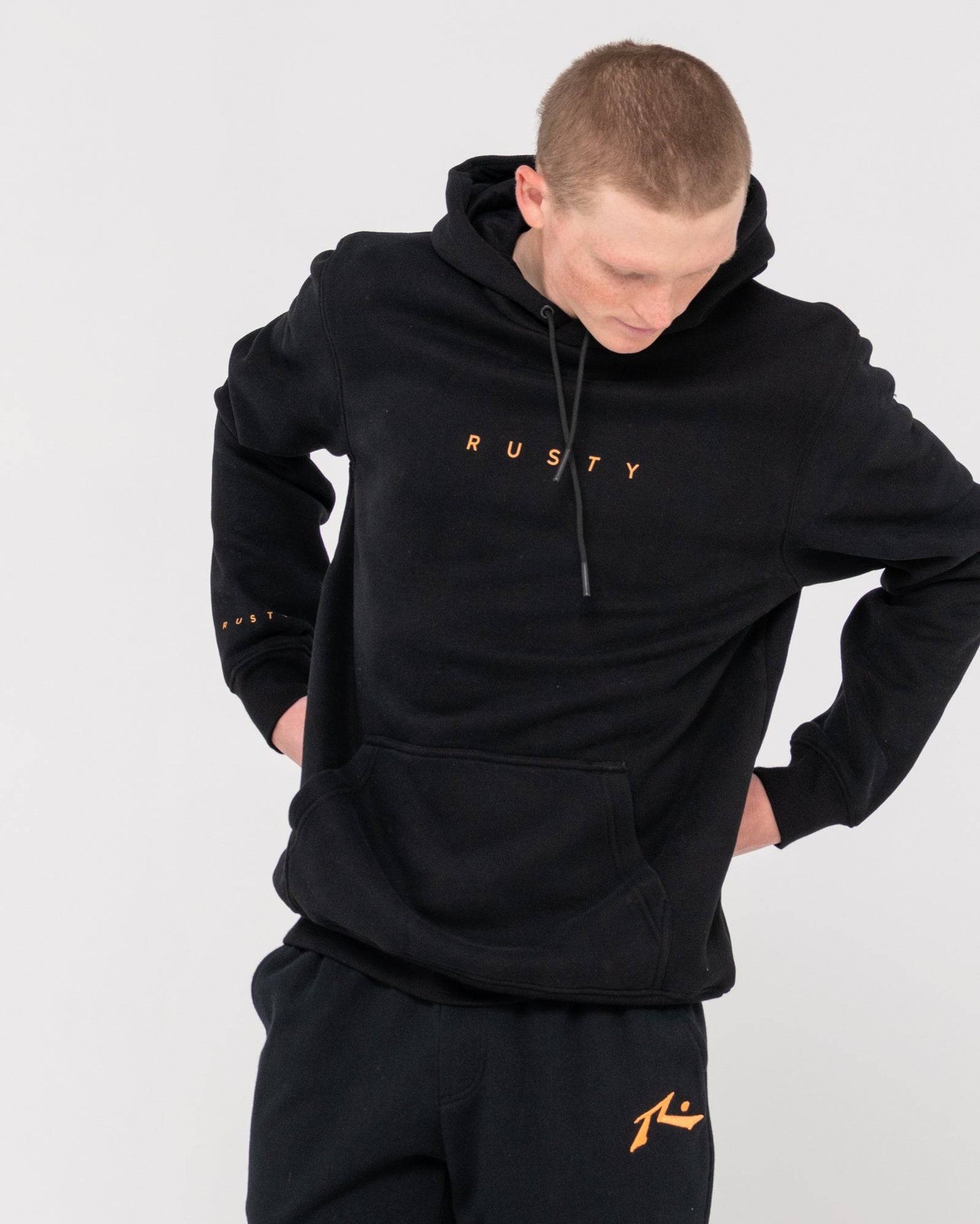 Rusty Short Hooded Fleece - Standard Fit Hoodie in black, shown with hands behind back, featuring front logo and kangaroo pocket.