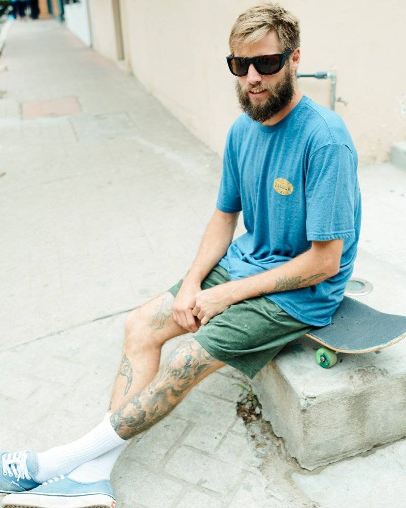 Man wearing I-sea Greyson 2.0 sunglasses sitting on a skateboard outdoors.
