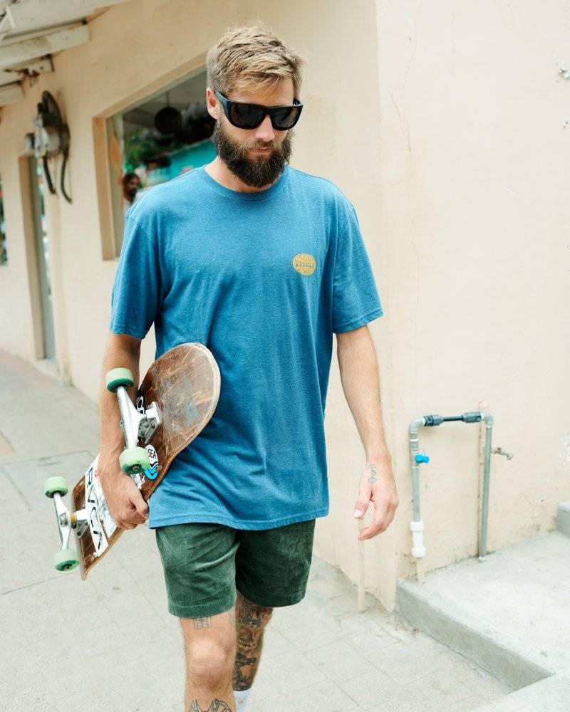 Man wearing I-sea Greyson 2.0 sunglasses holding a skateboard while walking outdoors.