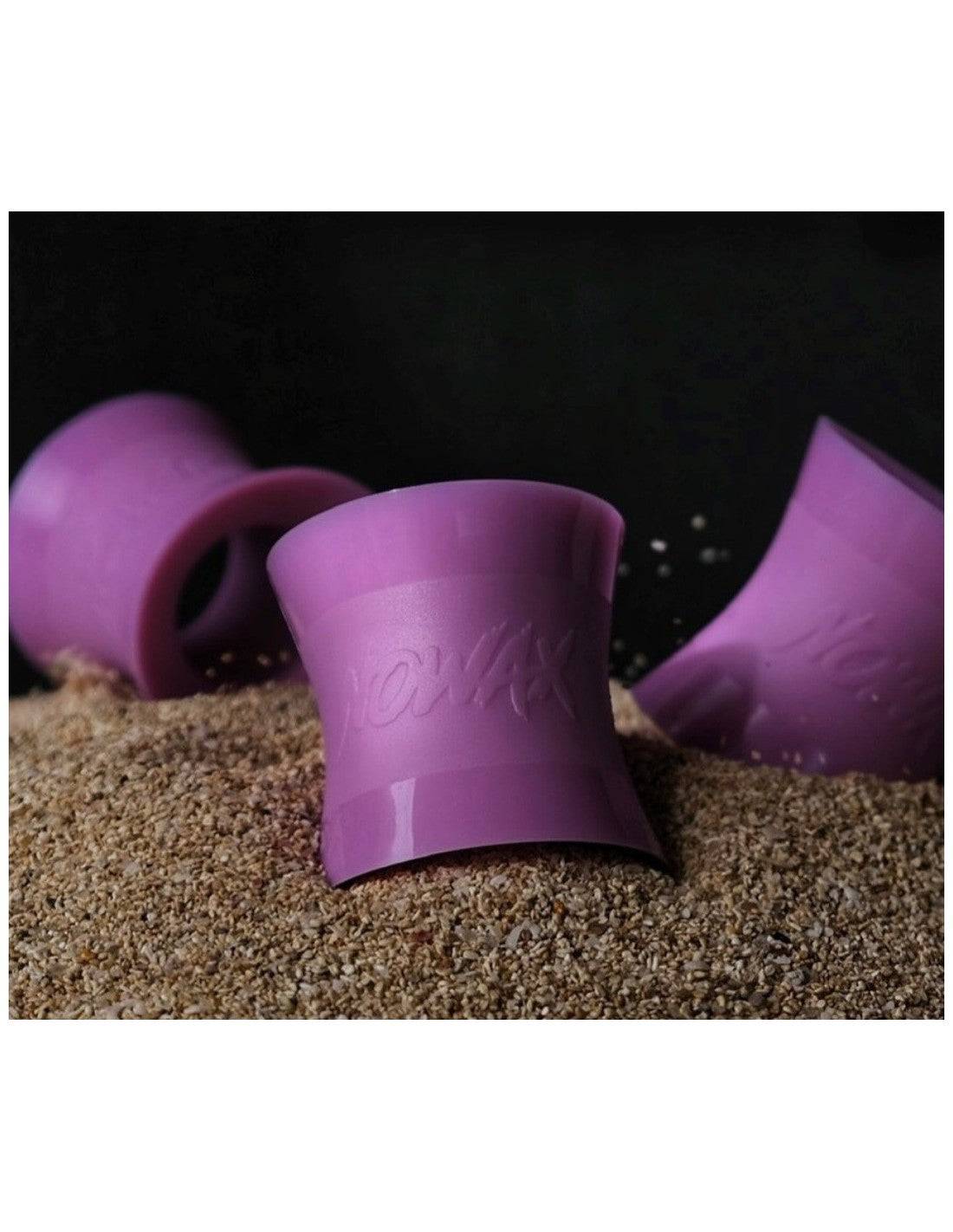 Purple NoWax surfboard wax removers displayed on sand, highlighting their durable and ergonomic design.